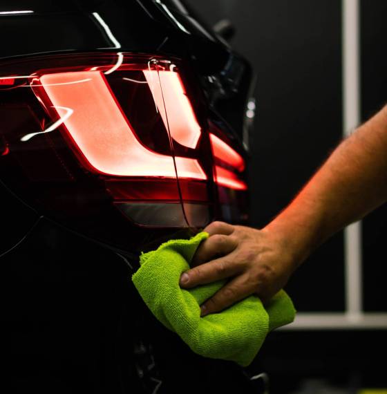 A selective focus shot of a man cleaning car's back headlight with a microfiber cloth